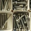 Close-up of various metal bolts stored in organized white bins.